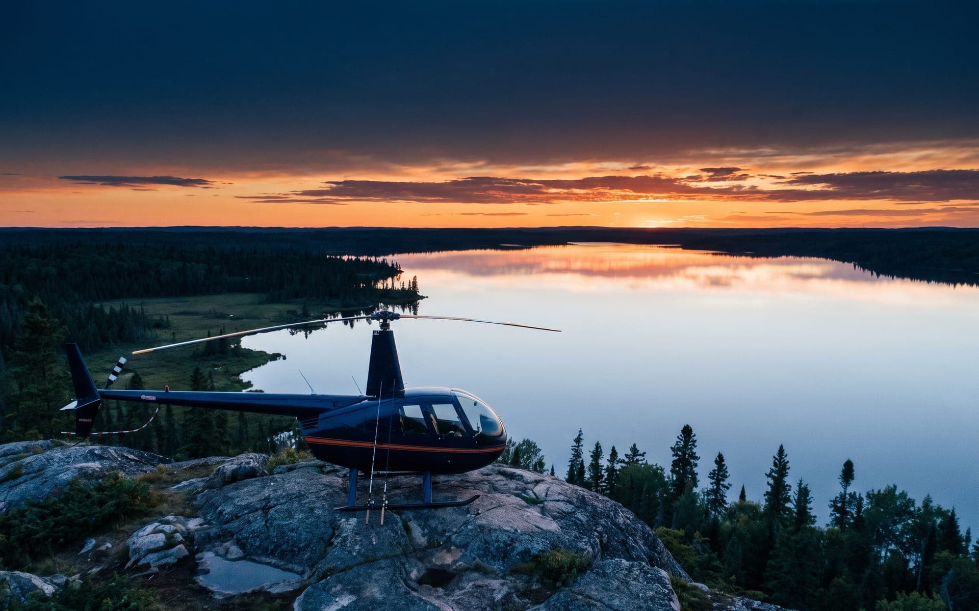 Helicopter on a granite point beside a vast mirror-calm lake at dusk