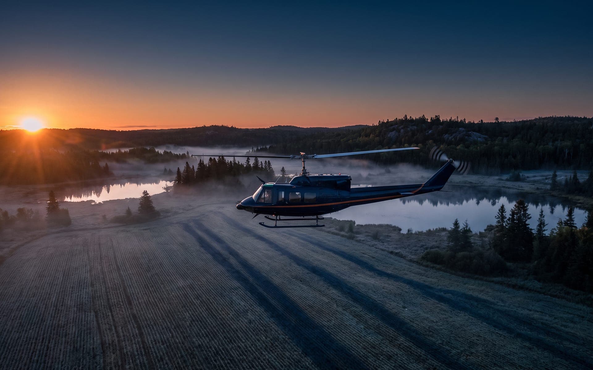 Helicopter flying low over misty farmland at sunrise
