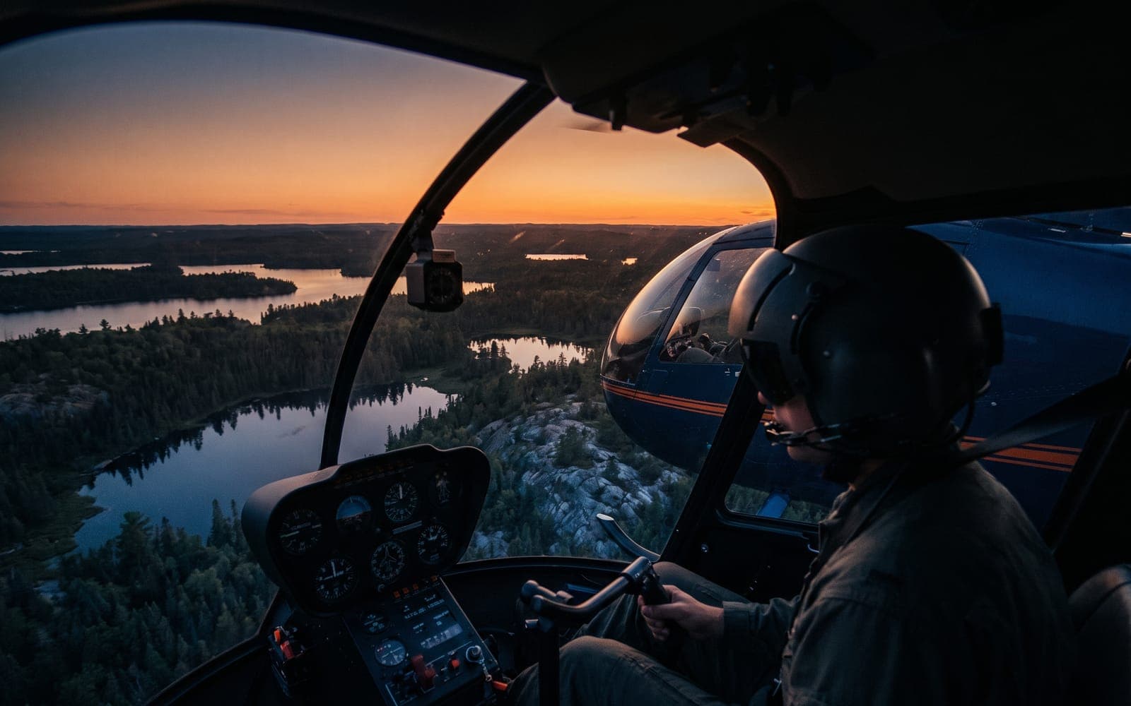 Helmeted pilot at the controls with dusk-lit lake country filling the windscreen
