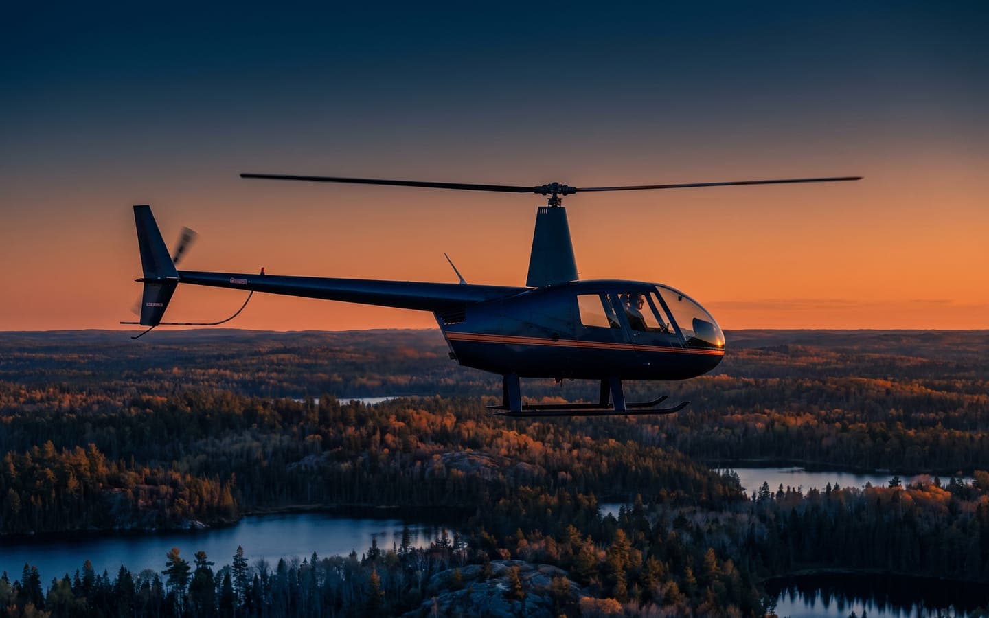 Light four-seat helicopter of the Robinson R44 type in flight over boreal forest (representative image)