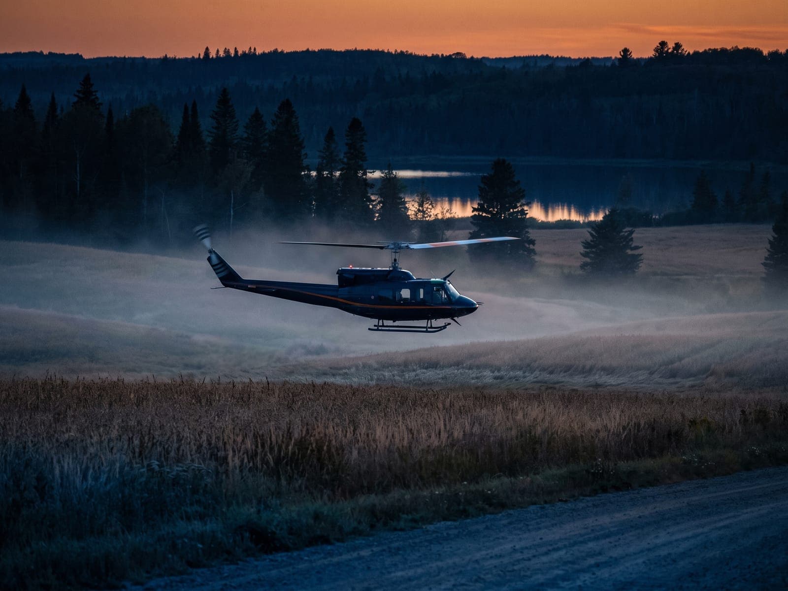 Helicopter making a low pass over misty farmland at dawn