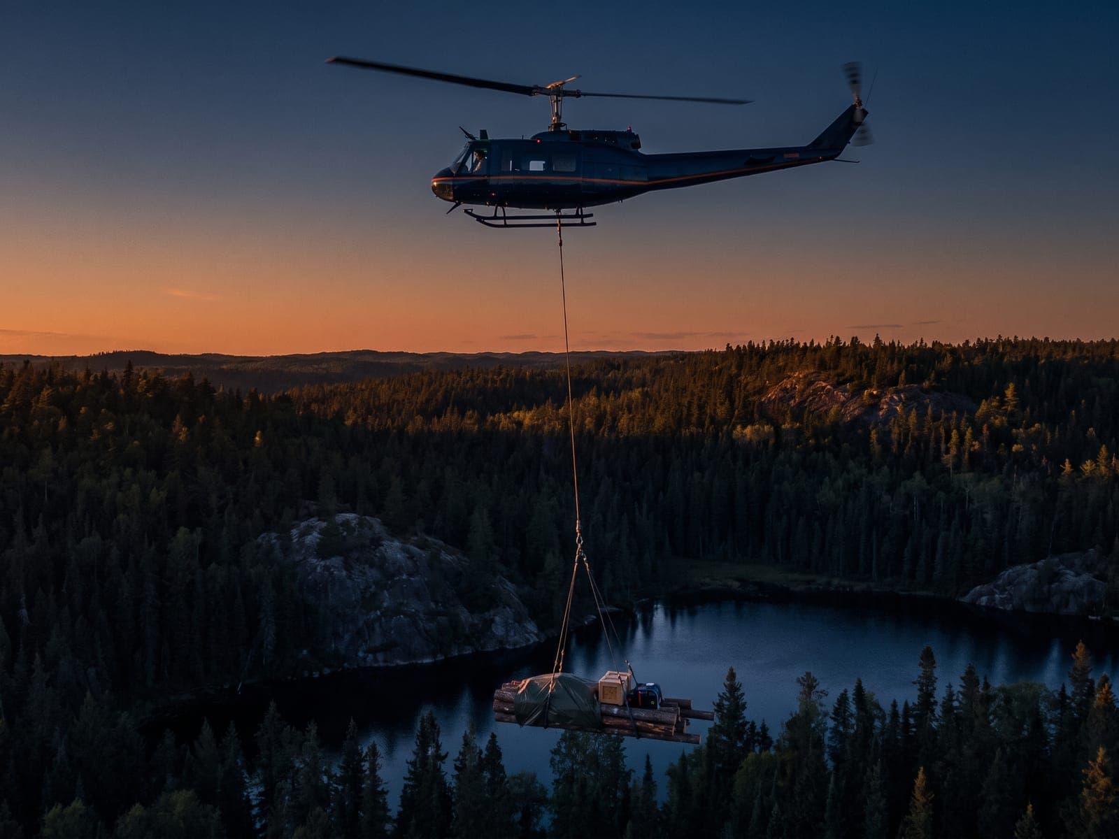 Helicopter flying a slung long-line load over boreal forest